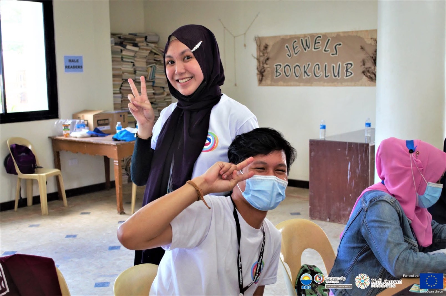 Two participants flash peace signs in front of a book club sign.