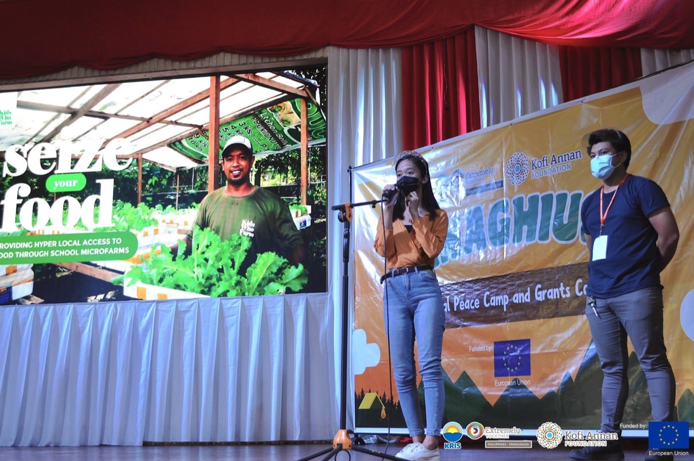 A youth participant presents a school microfarm project on stage.