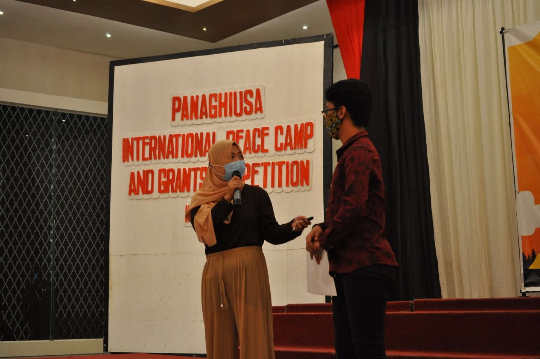 Facilitators speak on stage in front of the Panaghiusa banner.